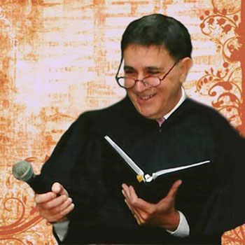 Rabbi Frank Tamburello, wearing glasses and clerical robes, holding a microphone and smiling